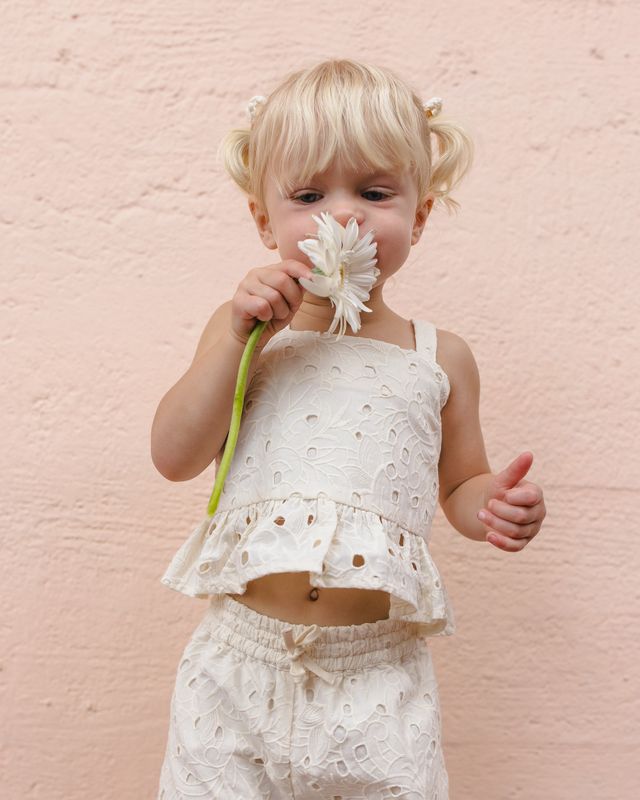Child in a white outfit holding a flower against a pink background