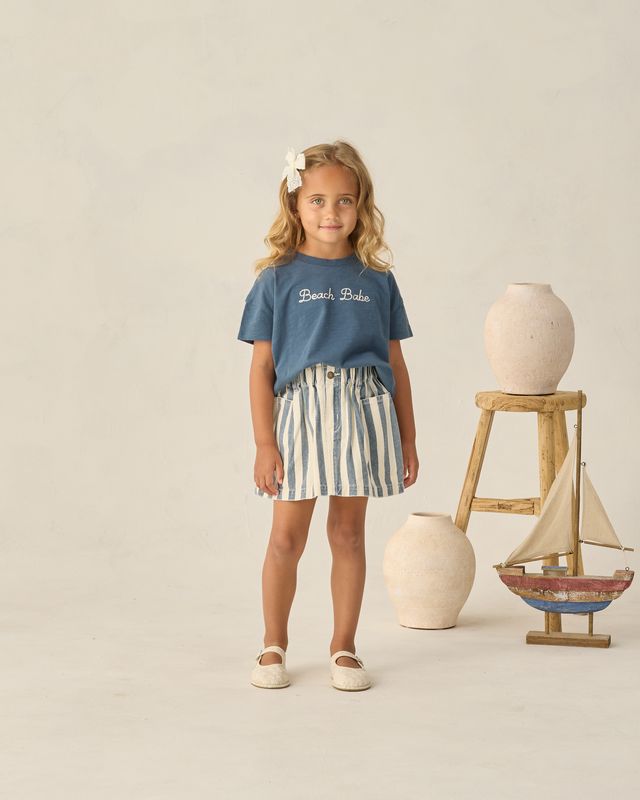 young girl wearing a navy tee and striped skirt 