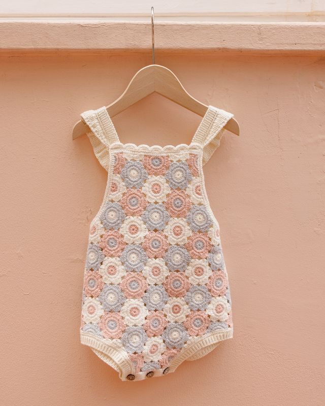 Baby romper with floral pattern on a hanger against a peach wall