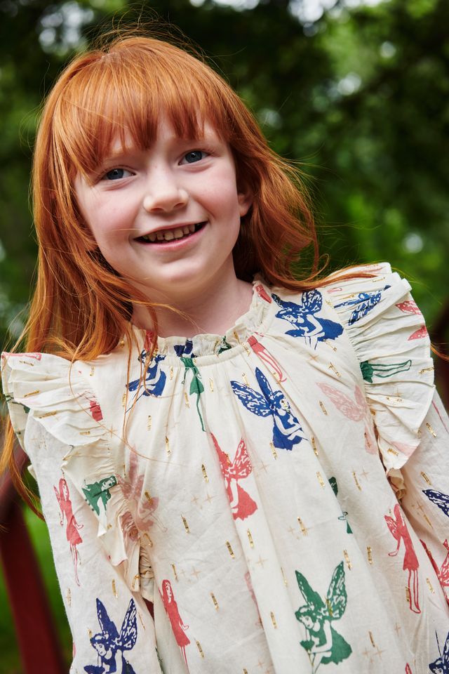 Young girl with red hair wearing a dress with fairy patterns outdoors.