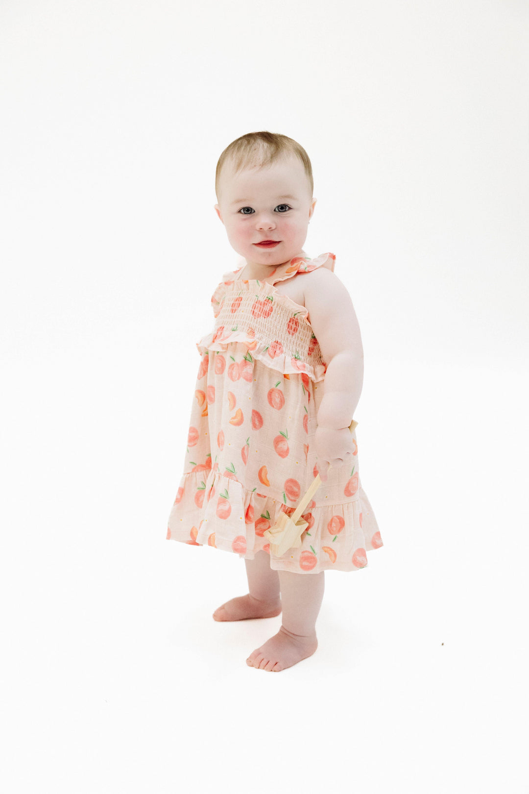 baby girl modeling the sweet peach dress. dress hits at the knee and has a smocked top. peaches and pieces of peaches all over the dress. 