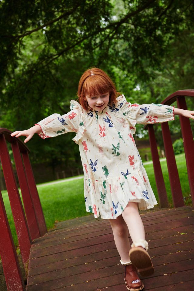Young girl in a dress with fairies on it standing on a wooden deck with greenery in the background