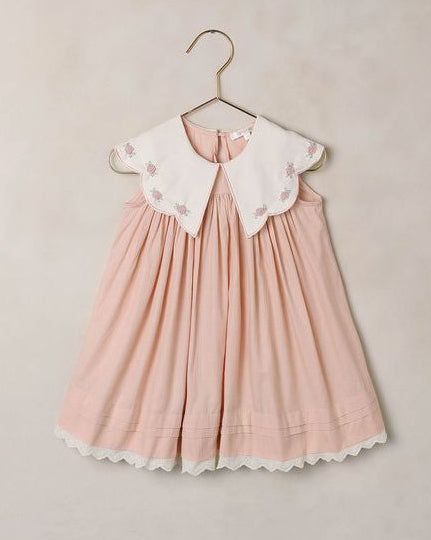 Pink dress with white collar on a hanger against a beige background