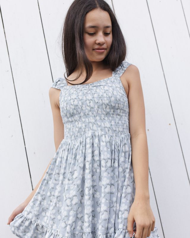 Young girl wearing a light blue floral dress against a white wooden background