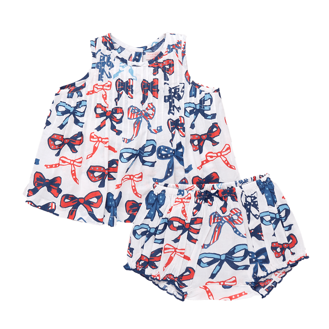 two piece baby outfit with blouse and bloomer, the blouse has a white round with bows that have a patriotic print in them: red, white and blue stripes and stars. 