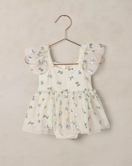 Beige dressiwith blue sequin bows on a hanger against a beige background