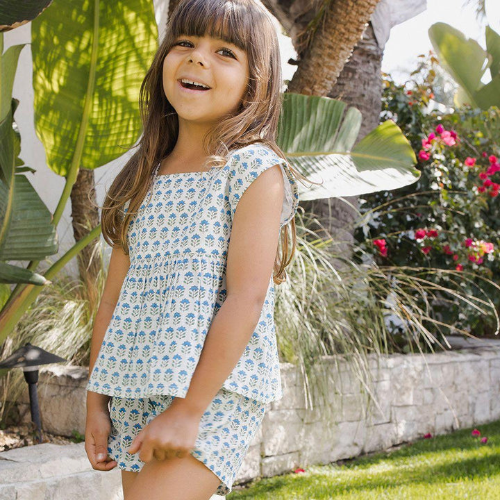 little girl modeling the short set. white with tiny blue flowers and green stem. cap sleeve with peplum bottom. 