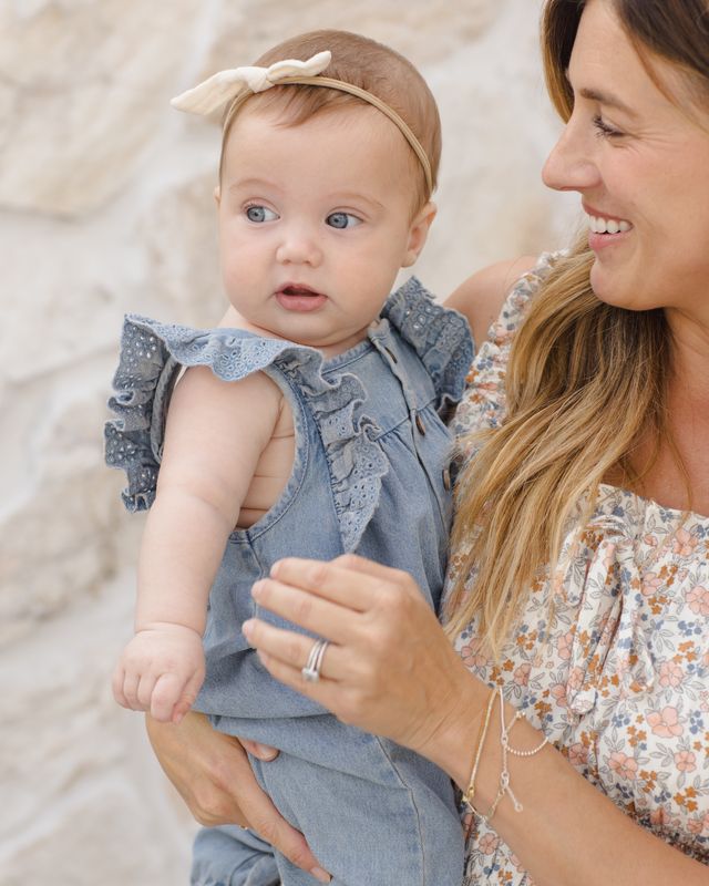 Woman holding a baby wearing a denim outfit with ruffled sleeves.