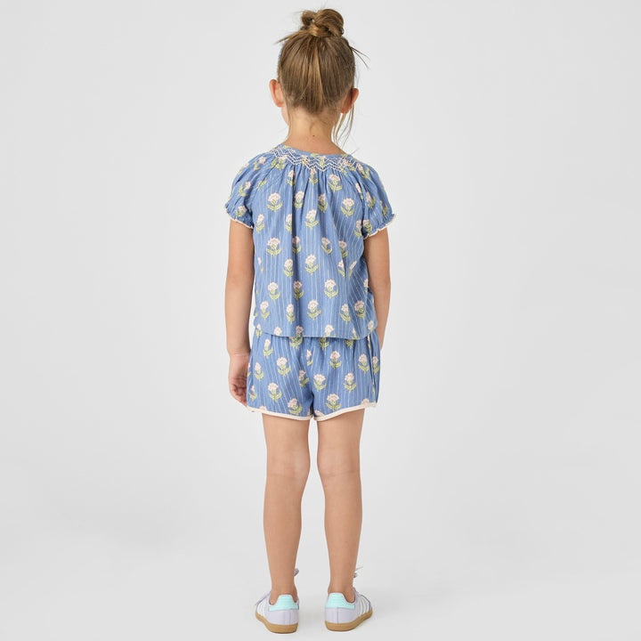 little girl modeling the periwinkle ava top and millie shorts set. this shows the top and shorts from the back. the top hits passed the waist and the shorts hit mid-thigh