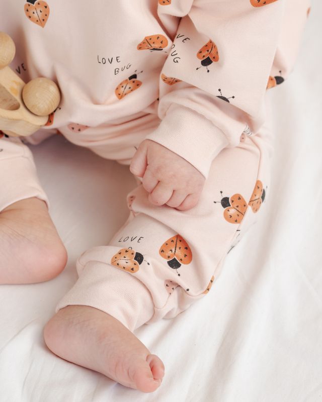 Baby's feet wearing pink pants with ladybug pattern on a white background