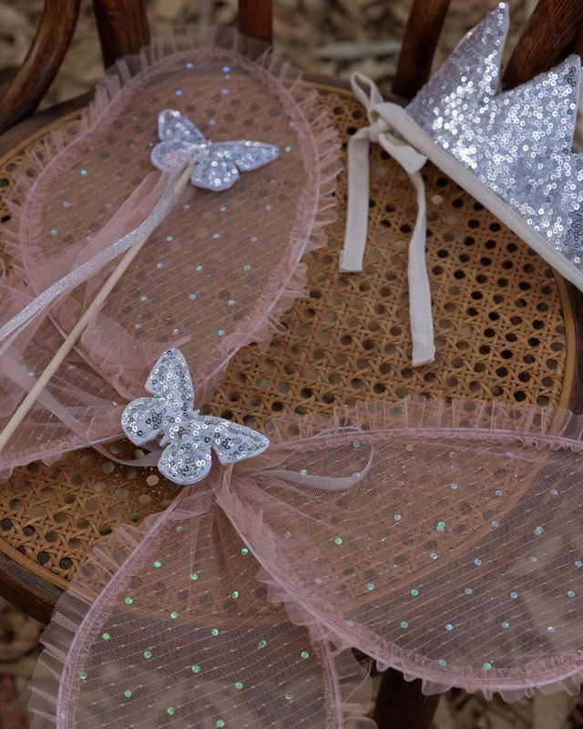 Butterfly-themed wings and wand with tulle and sequins on a wooden chair.