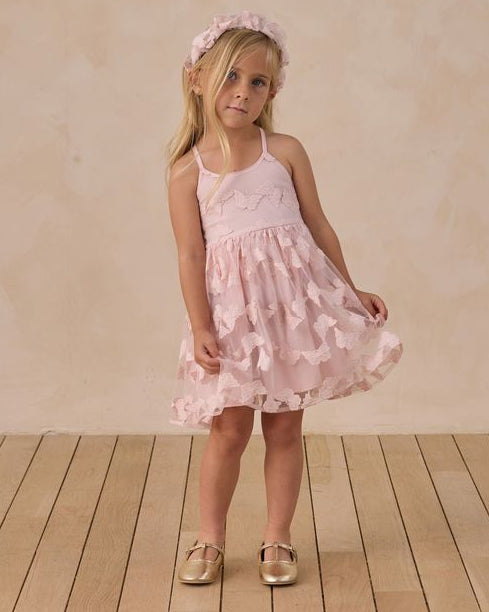 Young girl in a pink buttefly dress with tulle overlay standing on a wooden floor with a plain background