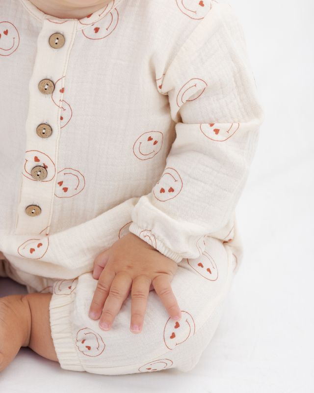Baby wearing a white outfit with smiley face patterns on a light background