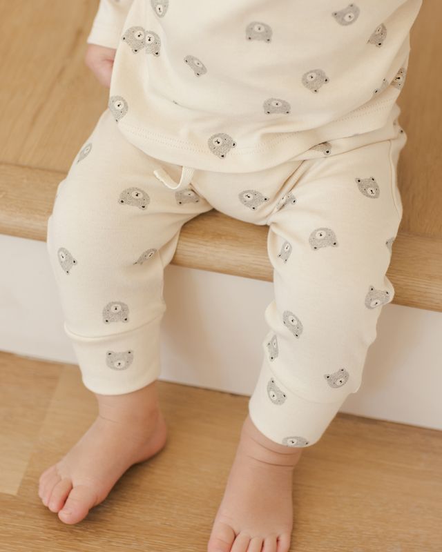 Baby wearing cream-colored pants with small gray bear patterns, sitting on a wooden surface.