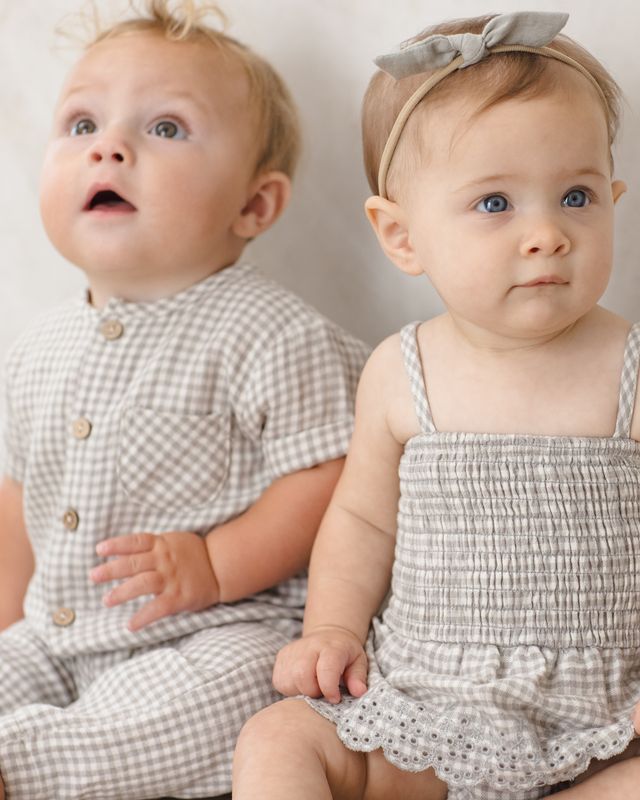 Two babies wearing matching outfits against a plain background