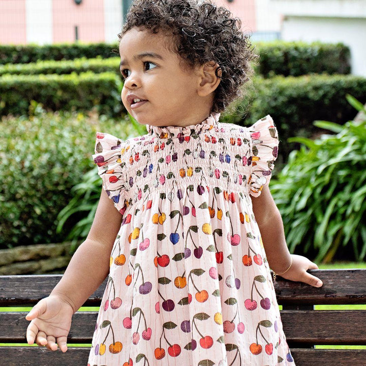 young girl modeling the stevie dress with cherry print all over the dress. high neck and ruffle at the sleeves 
