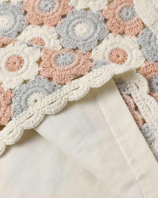Close-up of a crocheted two piece set with circular patterns in pastel colors on a white background.
