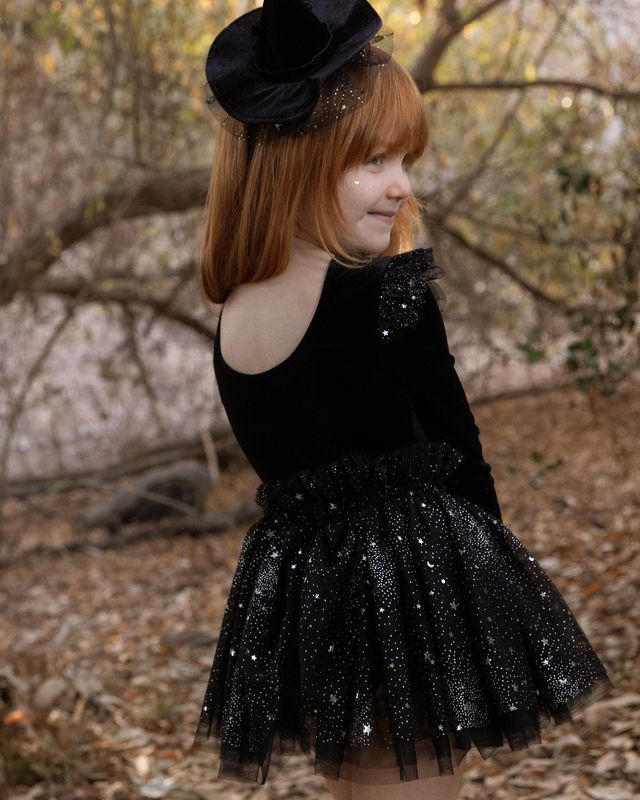 Young girl in a black dress with a sparkling skirt standing outdoors.