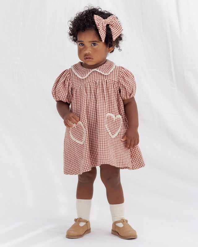 Young child wearing a red and white checkered dress with heart details on a white background