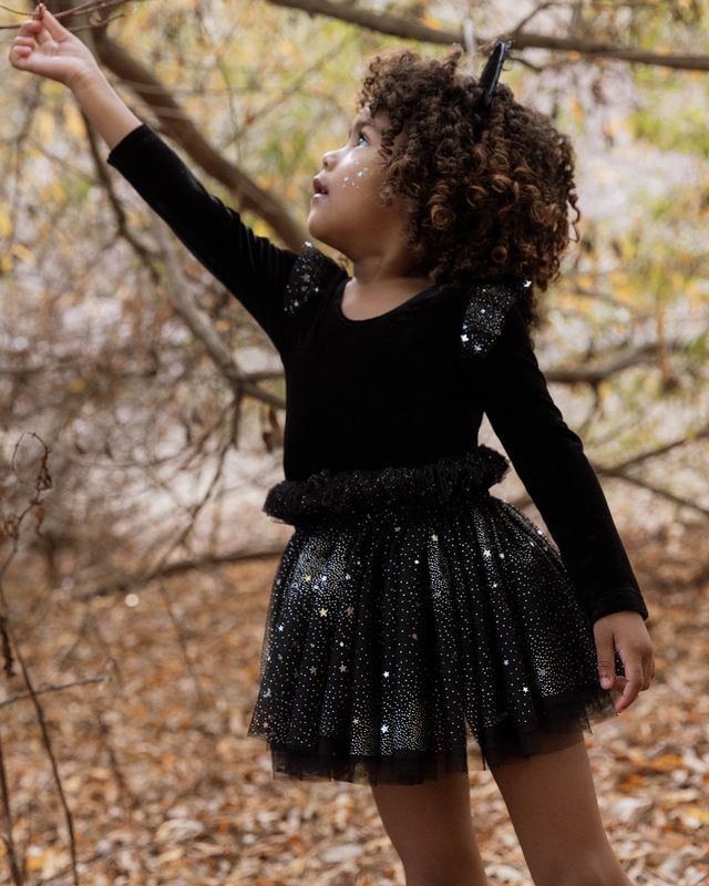 Child in a black outfit with sparkling details standing in a forest setting