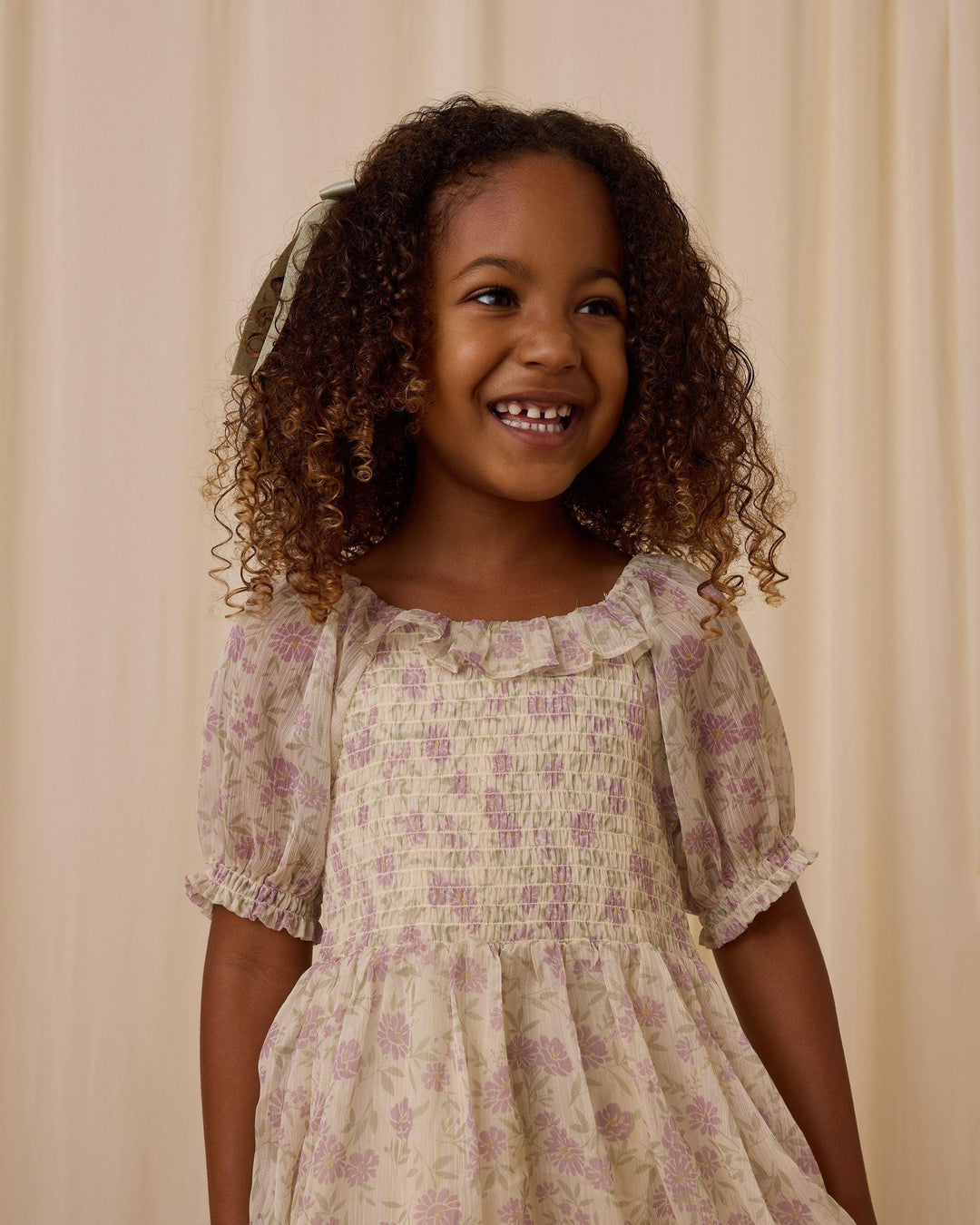 picture of a little girl wearing the chiffon dress with lavender floral pattern on the dress. up close picture of the smocking and ruffle at the collar. 