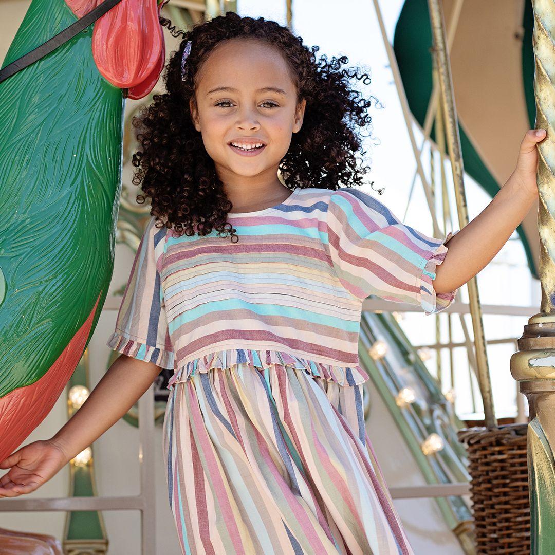 young girl models the stripe dress with the dress blowing in the wind. lots of movement in the dress. 