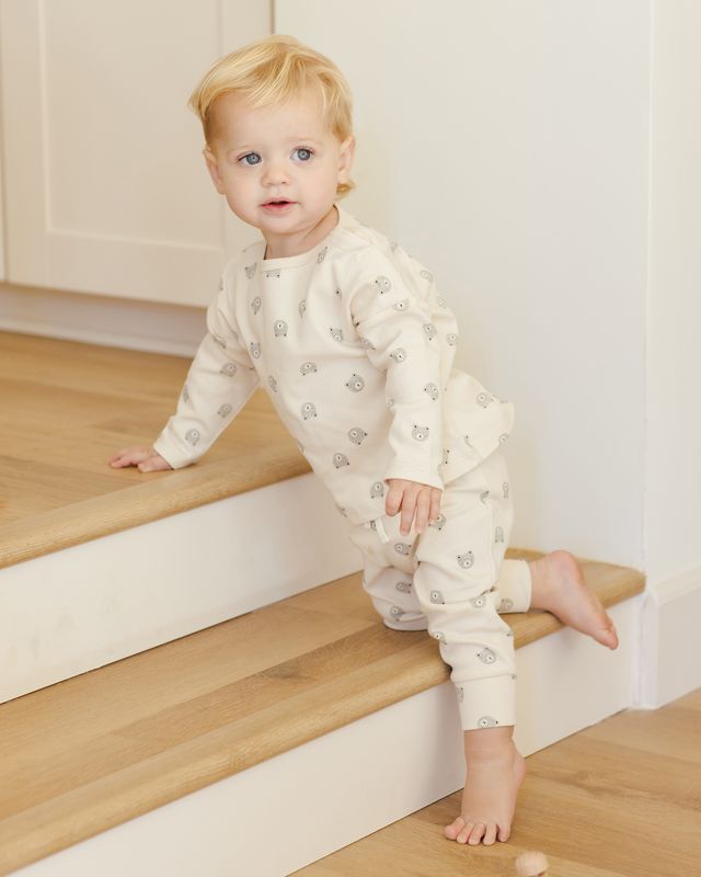 Child in a patterned two piece bear set kneeling on a staircase.