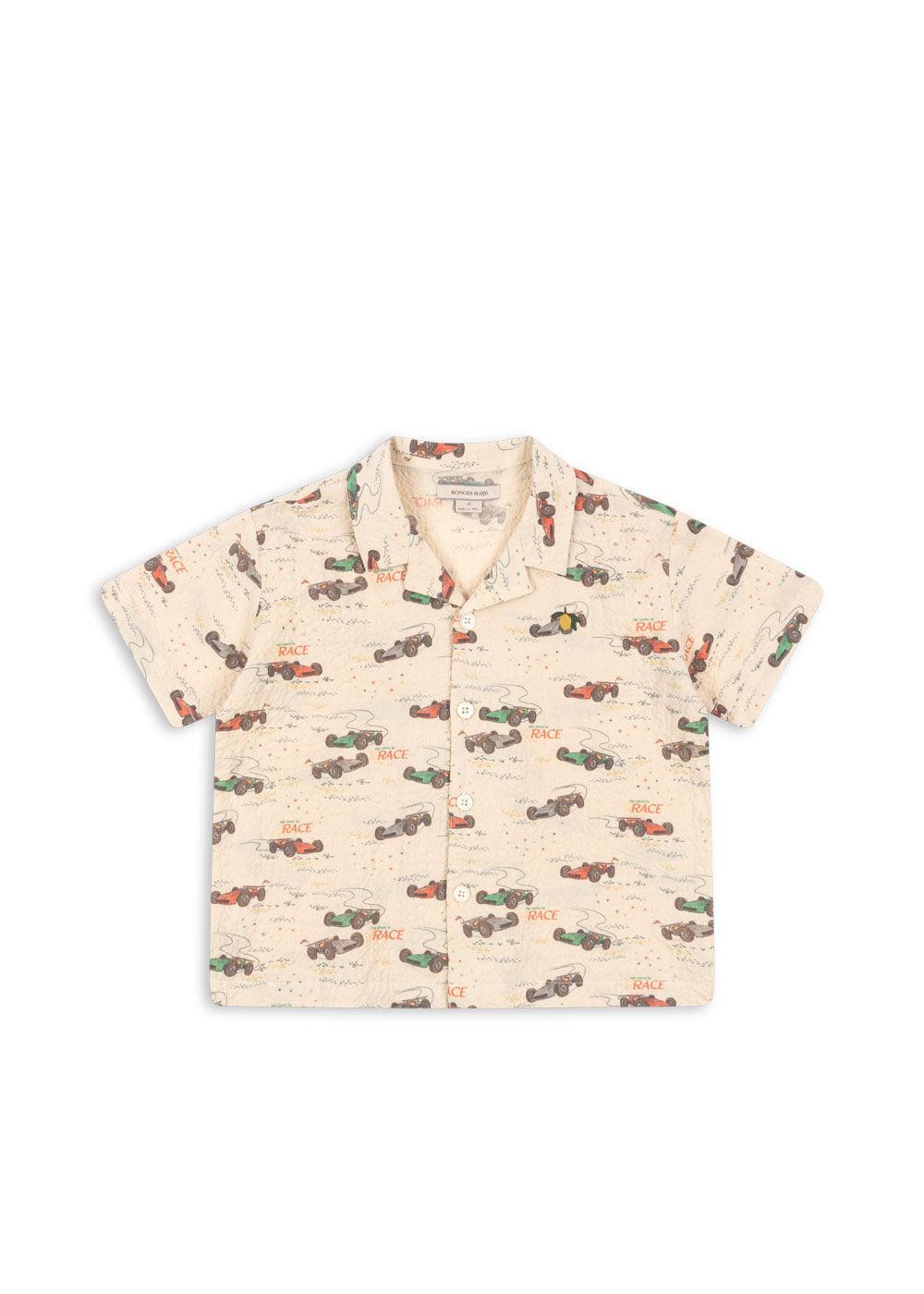 button down beige shirt with race cars in red, blue, green and gray all over the top. notches at each side of the collar. 