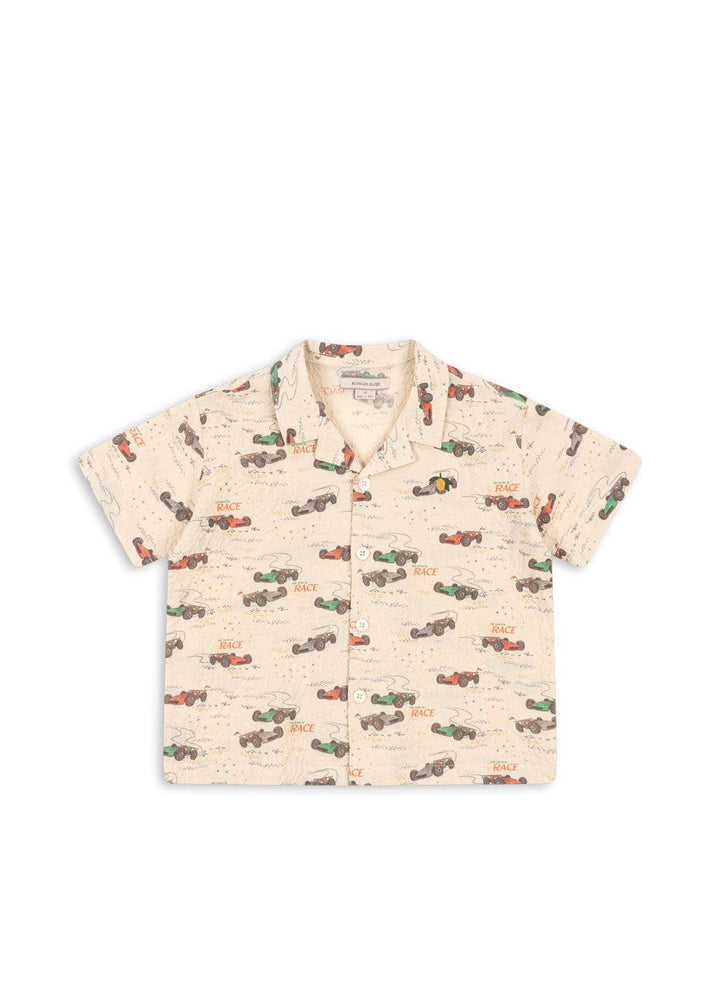 button down beige shirt with race cars in red, blue, green and gray all over the top. notches at each side of the collar. 