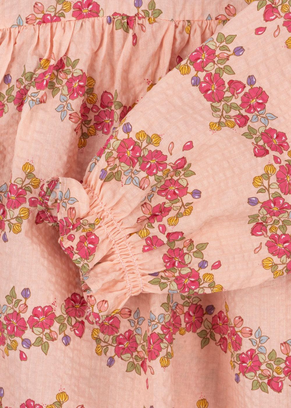 close up look of the pink romper with pretty florals all over and a delicate ruffle at the sleeve. 