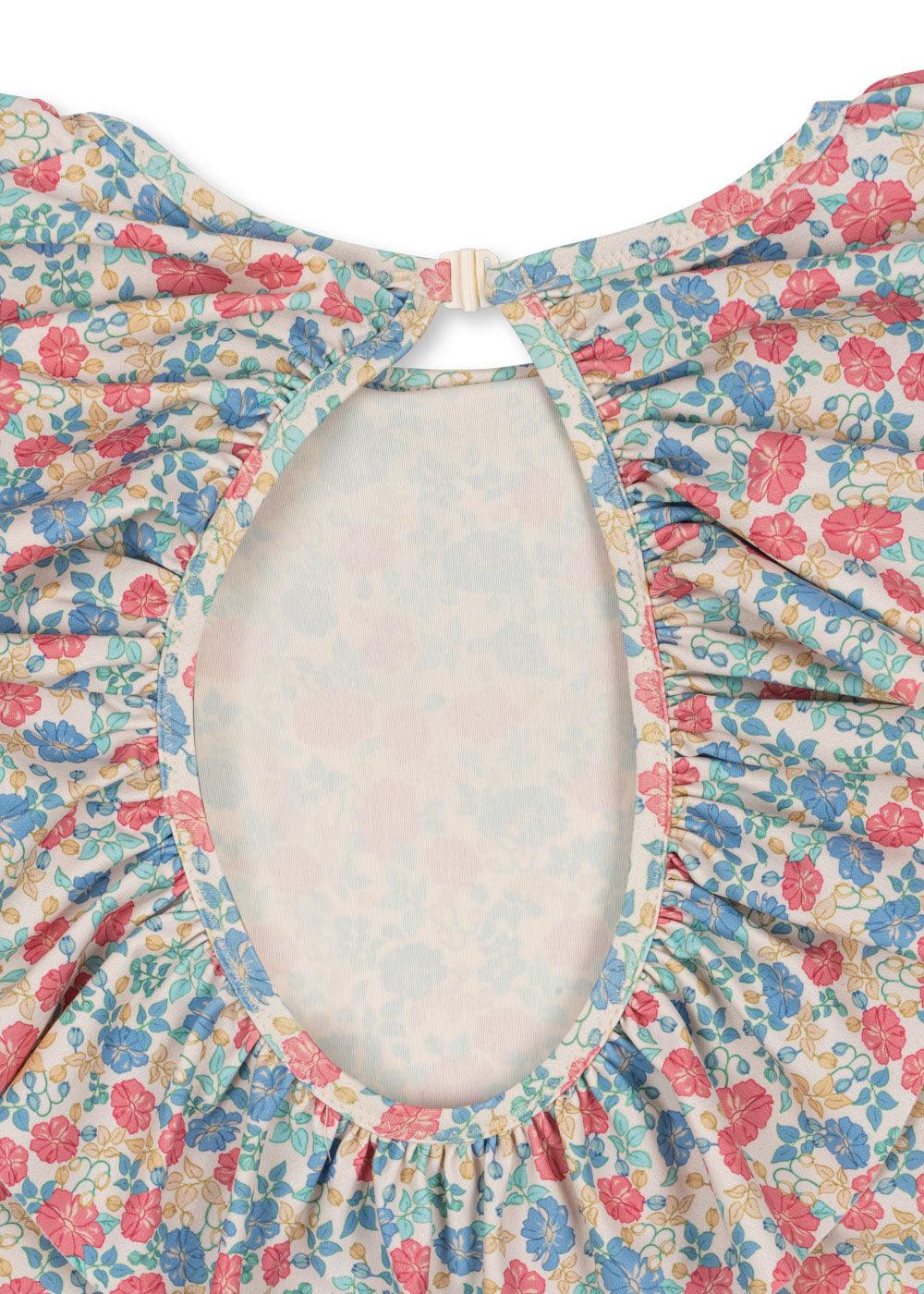 close up of the print and the cut out of the bathing suit. the print has blue, red/coral and beige floral print with ruffle around the opening. 