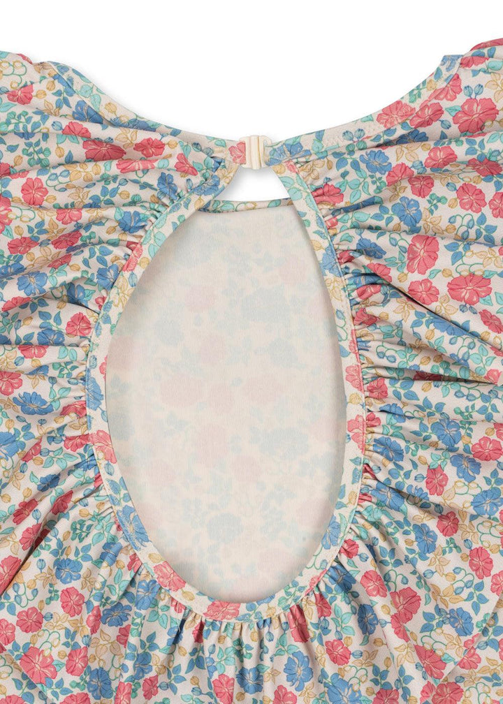 close up of the print and the cut out of the bathing suit. the print has blue, red/coral and beige floral print with ruffle around the opening. 