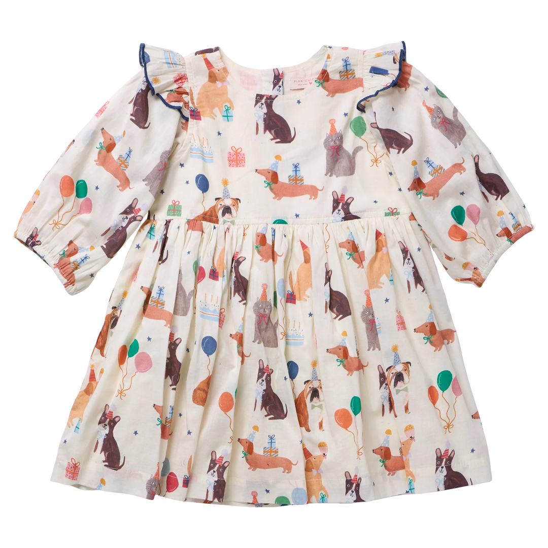 A baby girl's long-sleeve dress with a cream-colored base and an all-over print of dogs, cats and gifts, accented with blue ruffle trim at the shoulders.