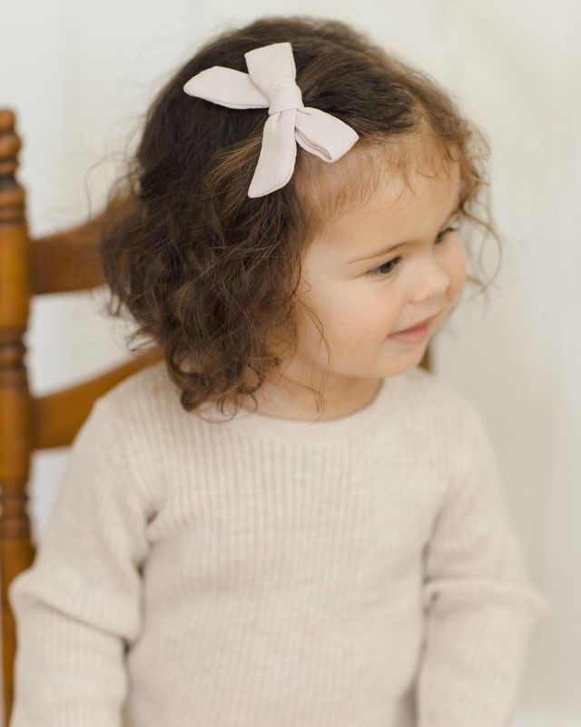 Child with a beige bow in their hair wearing a biege sweater.