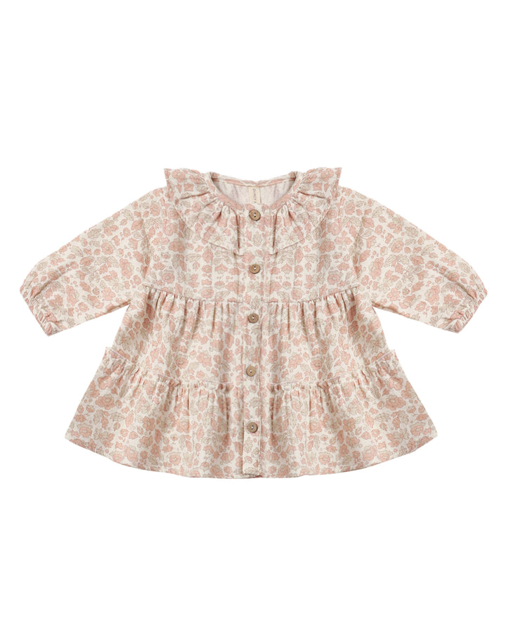 A long-sleeve baby girl's peplum blouse with a tiered skirt and button-front closure, featuring a light beige and dusty pink floral pattern.