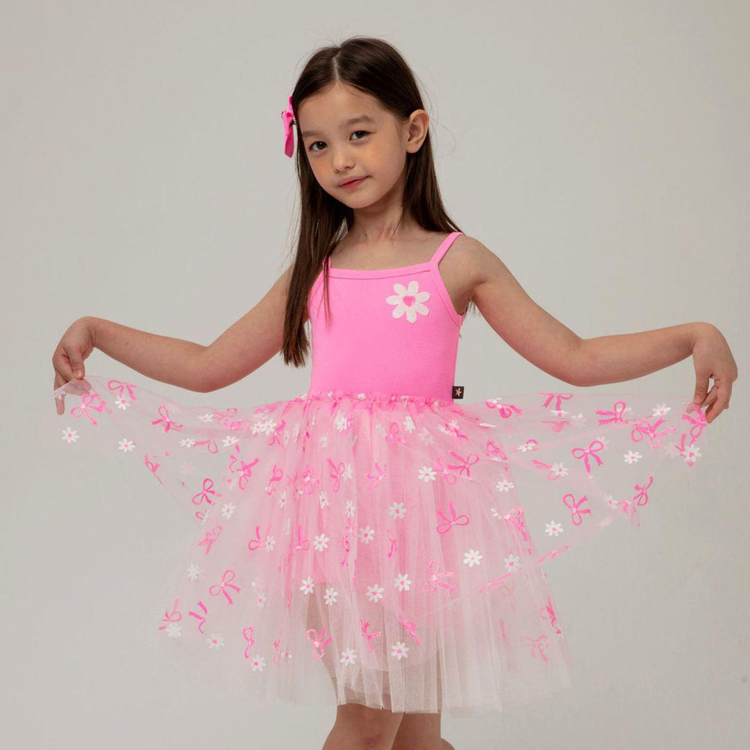 young girl modeling the hot pink tutu dress. the girl is pulling the tulle skirt up to see the details on the skirt better. 