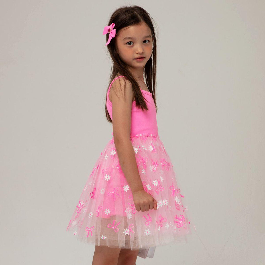 young girl modeling the pink dress with white tulle skirt with daisies and bows on the skirt. 