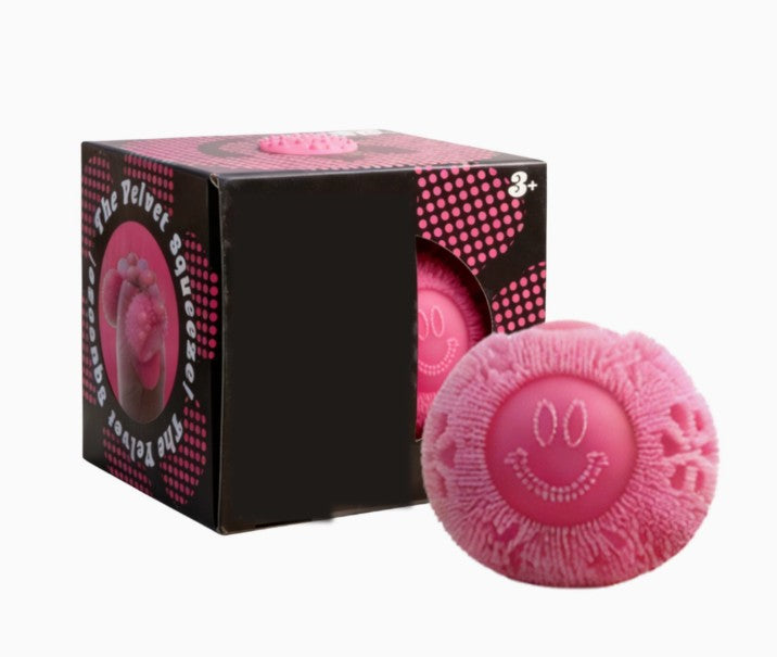 Pink textured squish ball with smiley face design next to its packaging on a white background