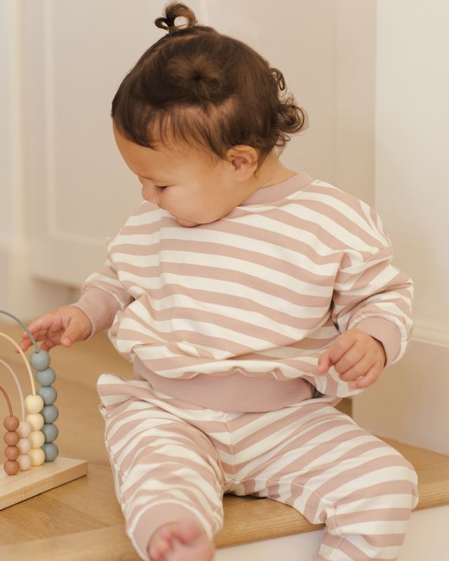 Child wearing a pink and white striped outfit sitting on a wooden step.