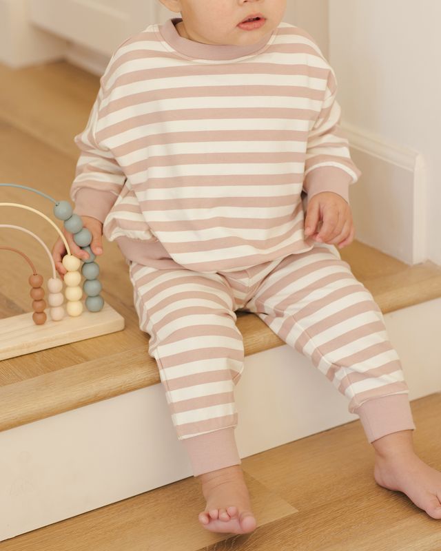 Child wearing pink and white striped pajamas sitting on a wooden step.