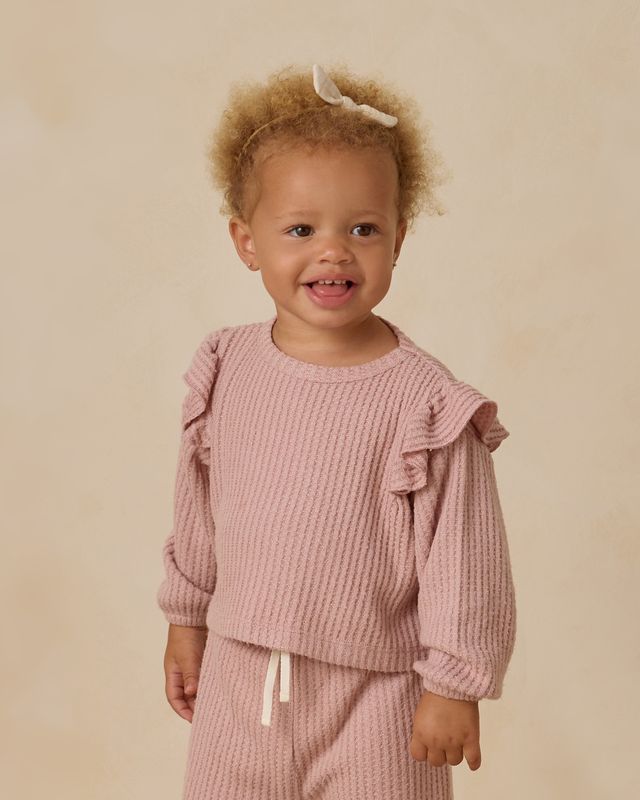 Child wearing a pink textured outfit with ruffled sleeves on a beige background