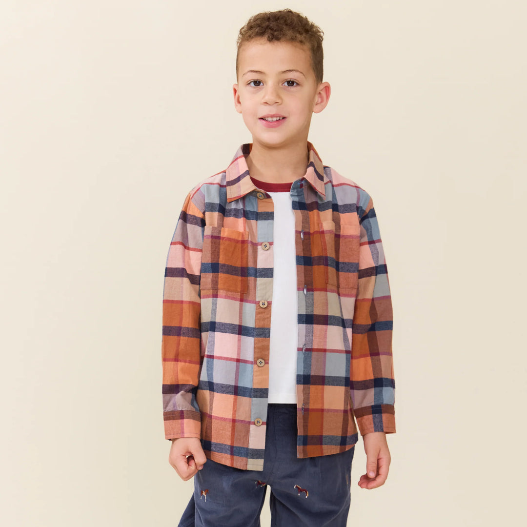 boy wearing a button down open with a white tee underneath. the button down is the color of a rust plaid . 