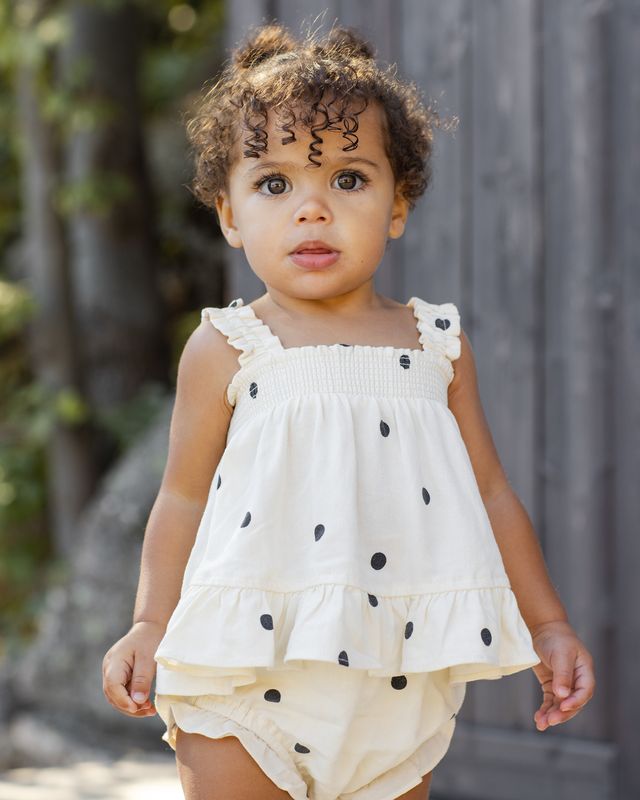 Child wearing a white top with black polka dots and white and black polka dots outdoors.