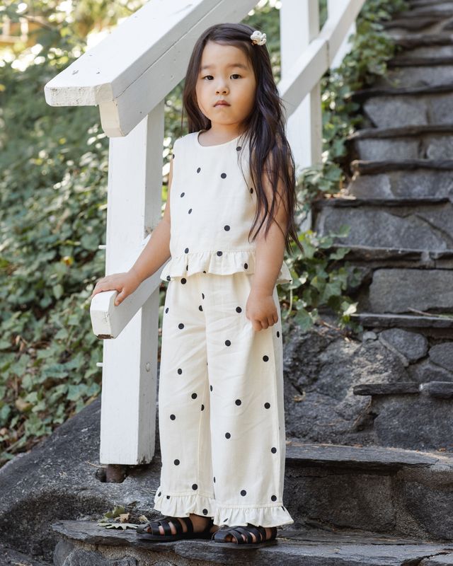 Young girl in a polka dot 2 piece outfit standing on stone steps outdoors.