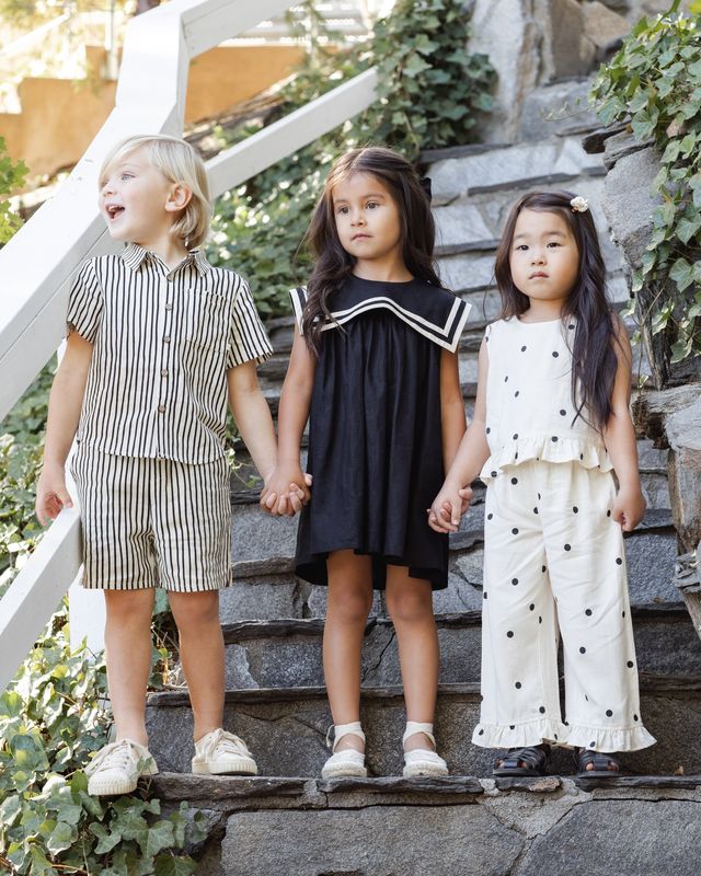 Three children holding hands on stone steps outdoors
