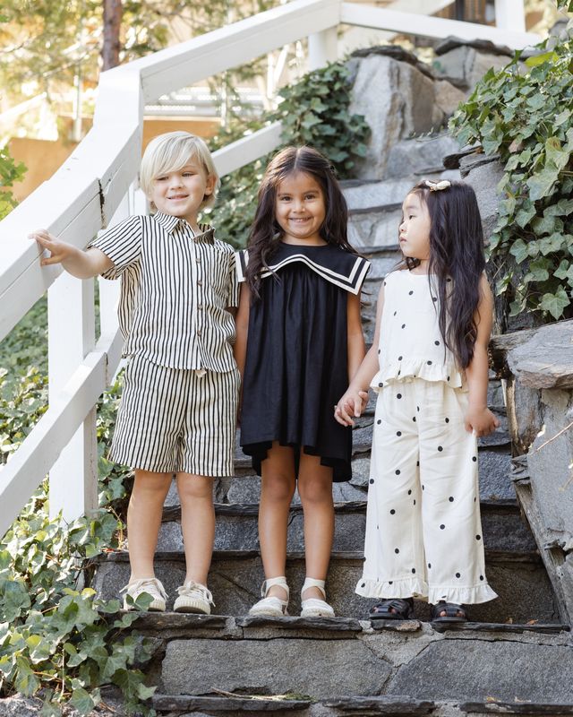 Three children standing on stone steps outdoors, wearing summer clothing.