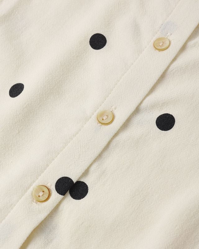 close up of the ivory fabric with black polka dots all over with buttons on the back. 