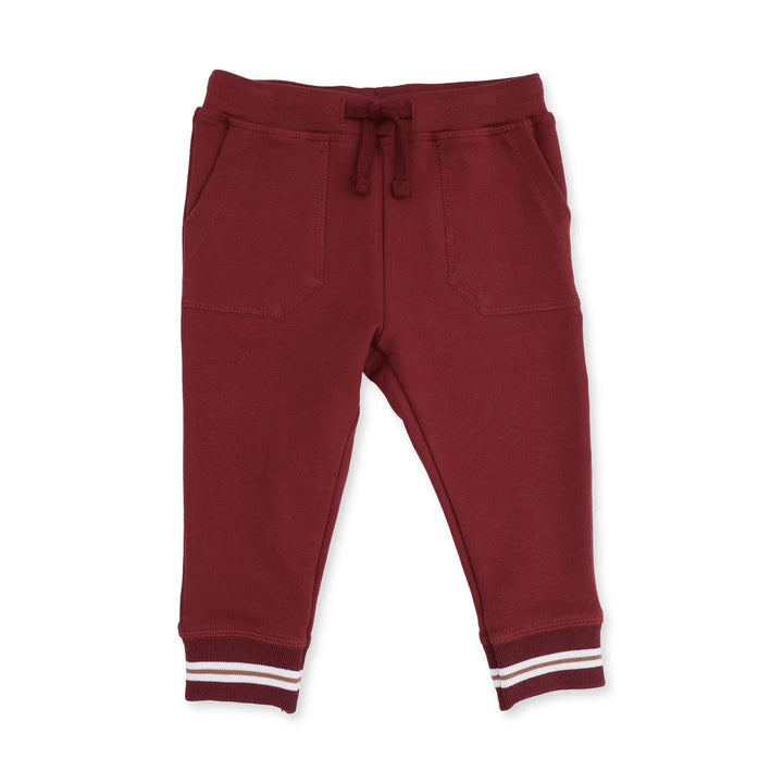 A pair of toddler jogger pants in burgundy, featuring an elastic waistband with a matching drawstring, side pockets, and ribbed ankle cuffs with white stripes.