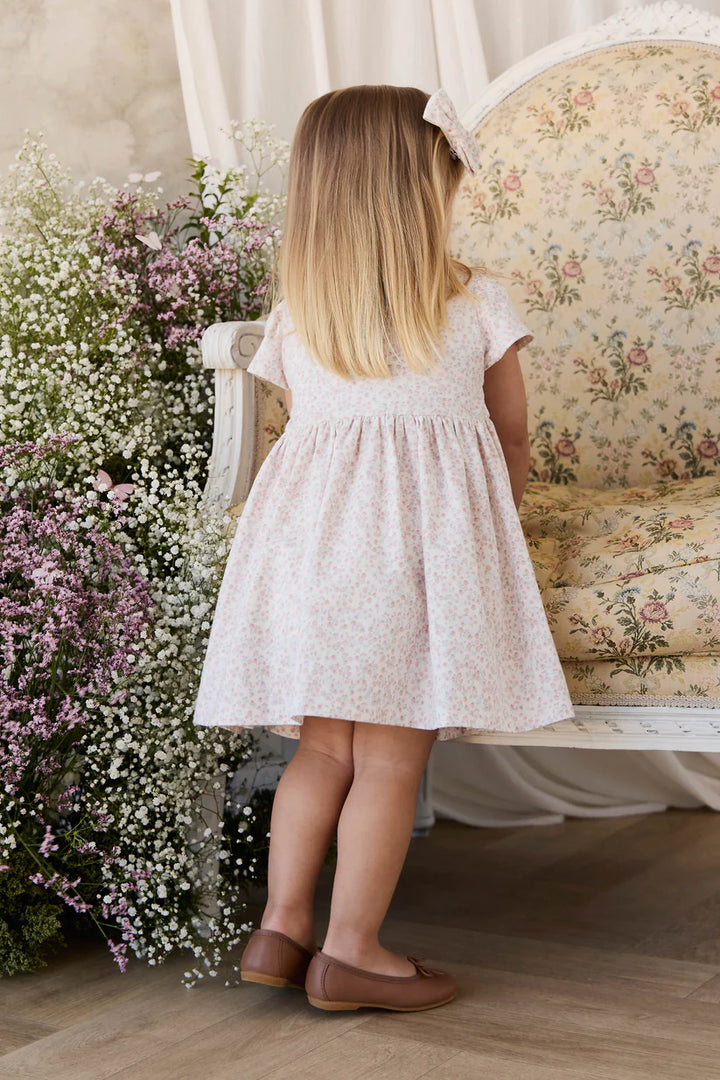 Young girl in a floral dress standing next to a floral arrangement in a room with vintage furniture.