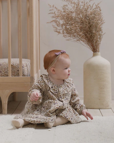 baby modeling the posy dress while sitting on the floor. has a nice room fit on the baby. 